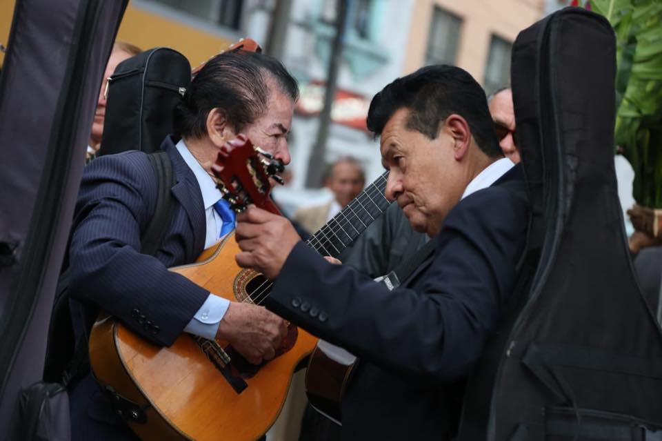 Grupo de guitarristas de trío posa y tocan en la avenida, con estuches e instrumentos visibles. Mienbros de La Playa Vive.